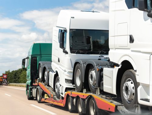 Back view of semi-trailer flatbed vehicle deliverying many new electric trucks sale automotive dealer from factory plant on highway interstate road. New business cargo transport fleet export import.