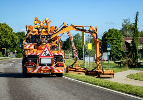 Tractor with a mechanical mower mowing grass on the side of the asphalt road. Road services are engaged in landscaping around roads.